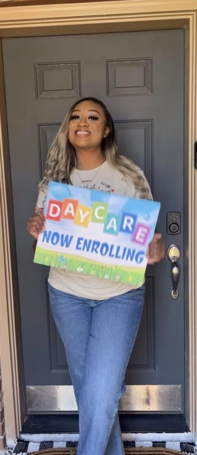 Ms. Chelsey holding a Daycare Now Enrolling sign